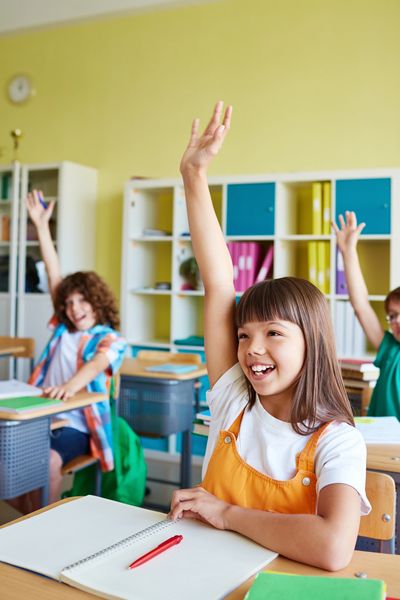 Girl raising her hand in class with two other students. 