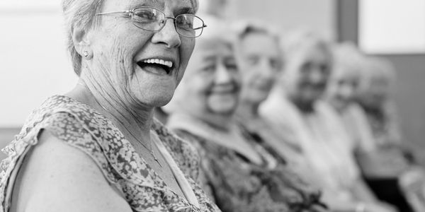 Smiling elderly woman with a group of seniors in a line, black and white photo.