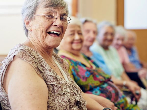 Smiling elderly woman sitting with a group of seniors in a cheerful setting.