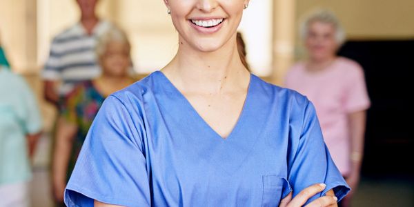 Smiling female healthcare worker with elderly patients in background.