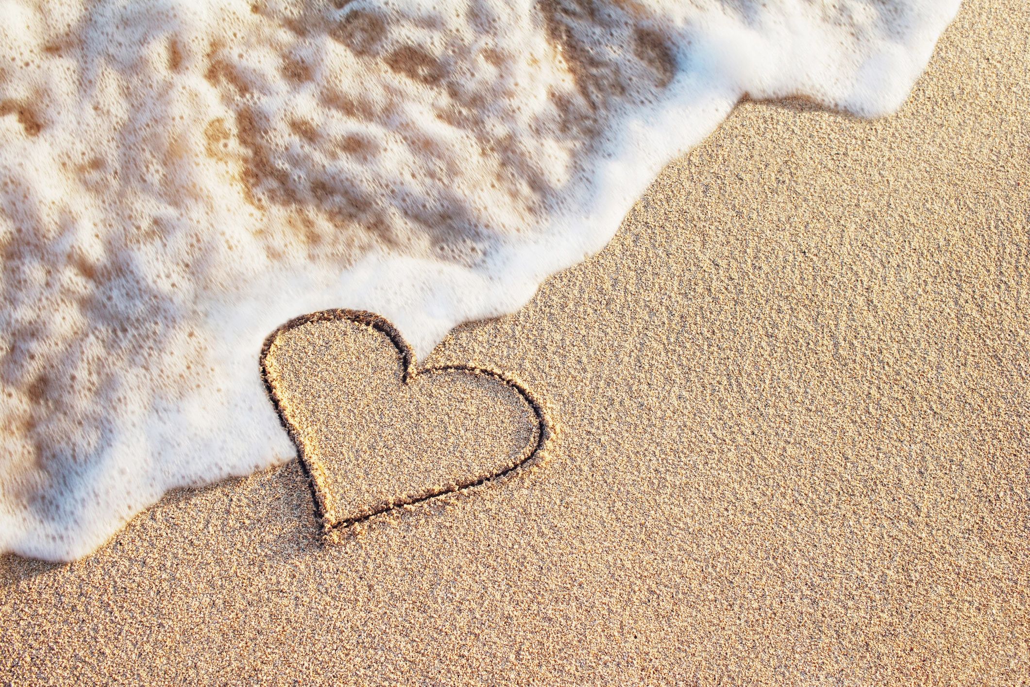 A heart drawn on the beach sand near gentle ocean waves.