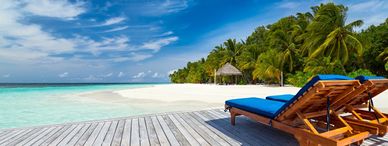 Two blue-cushioned wooden lounge chairs on a tropical beach deck.