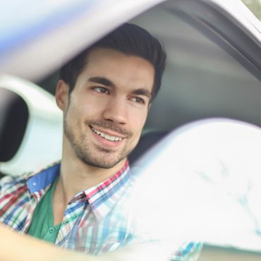Smiling young man sitting in a car looking out the window.