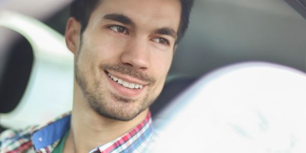 Smiling man sitting in a car, looking out the window.
