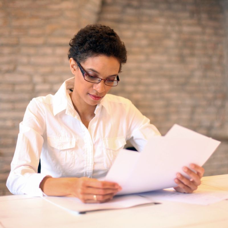 Mixed race mid adult woman, office worker examining documents in an office. About 30 years old, smiling woman with short curly hair.