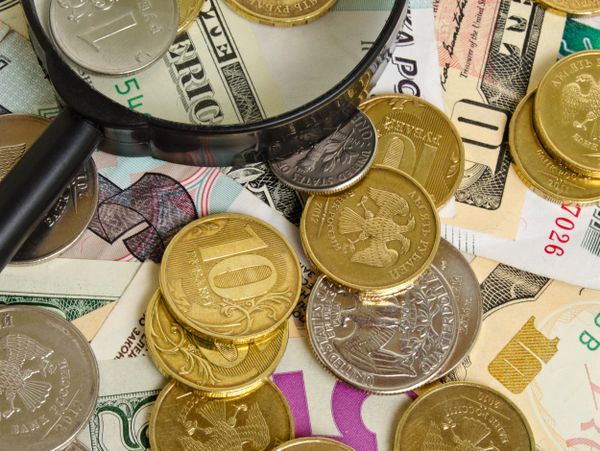 Magnifying glass over mixed currency coins and bills.