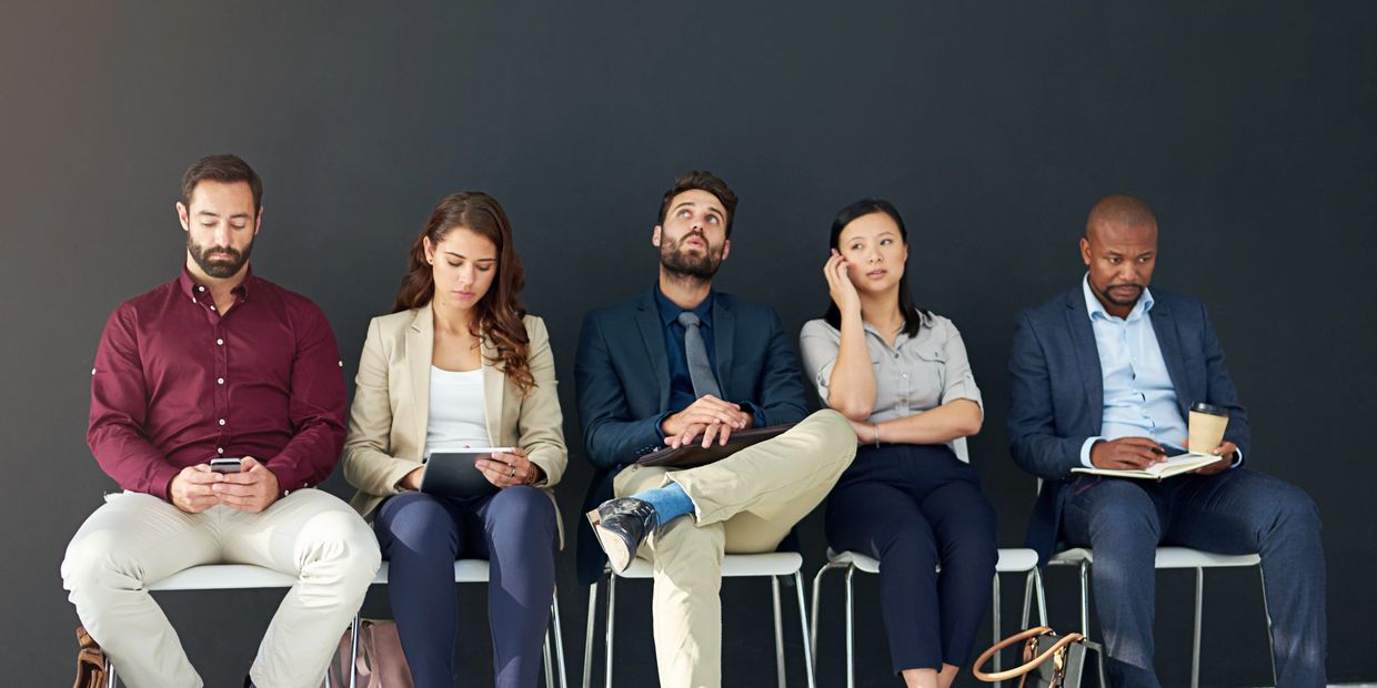 Five diverse professionals waiting, engaged with devices and notes.