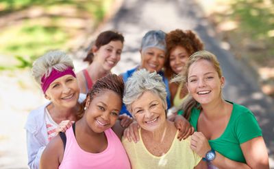 A diverse group of smiling women outdoors enjoying a sunny day together.