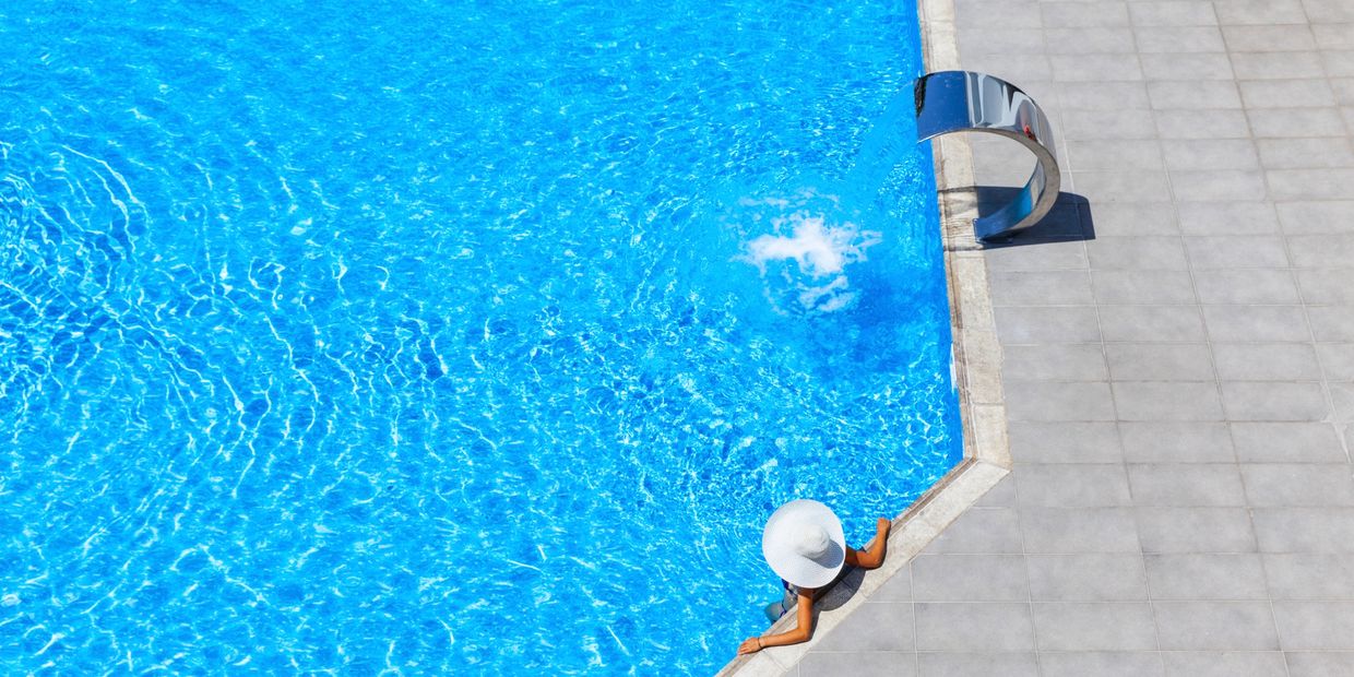 Person relaxing in a pool wearing a white sunhat on a sunny day.