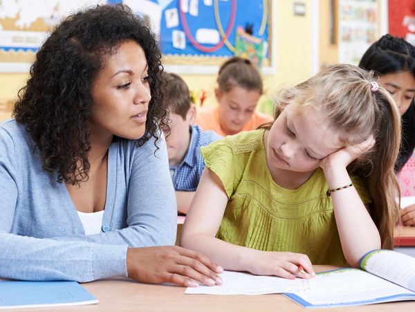 This image shows a teacher sitting next to a young girl in a classroom.