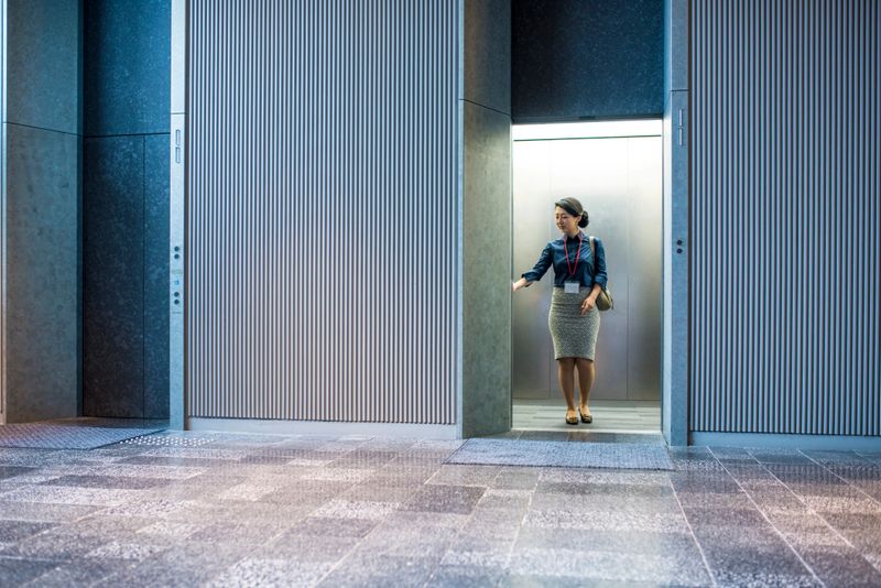 Japanese businesswoman standing in elevator, waiting for doors to close. She is pushing the button to go up.