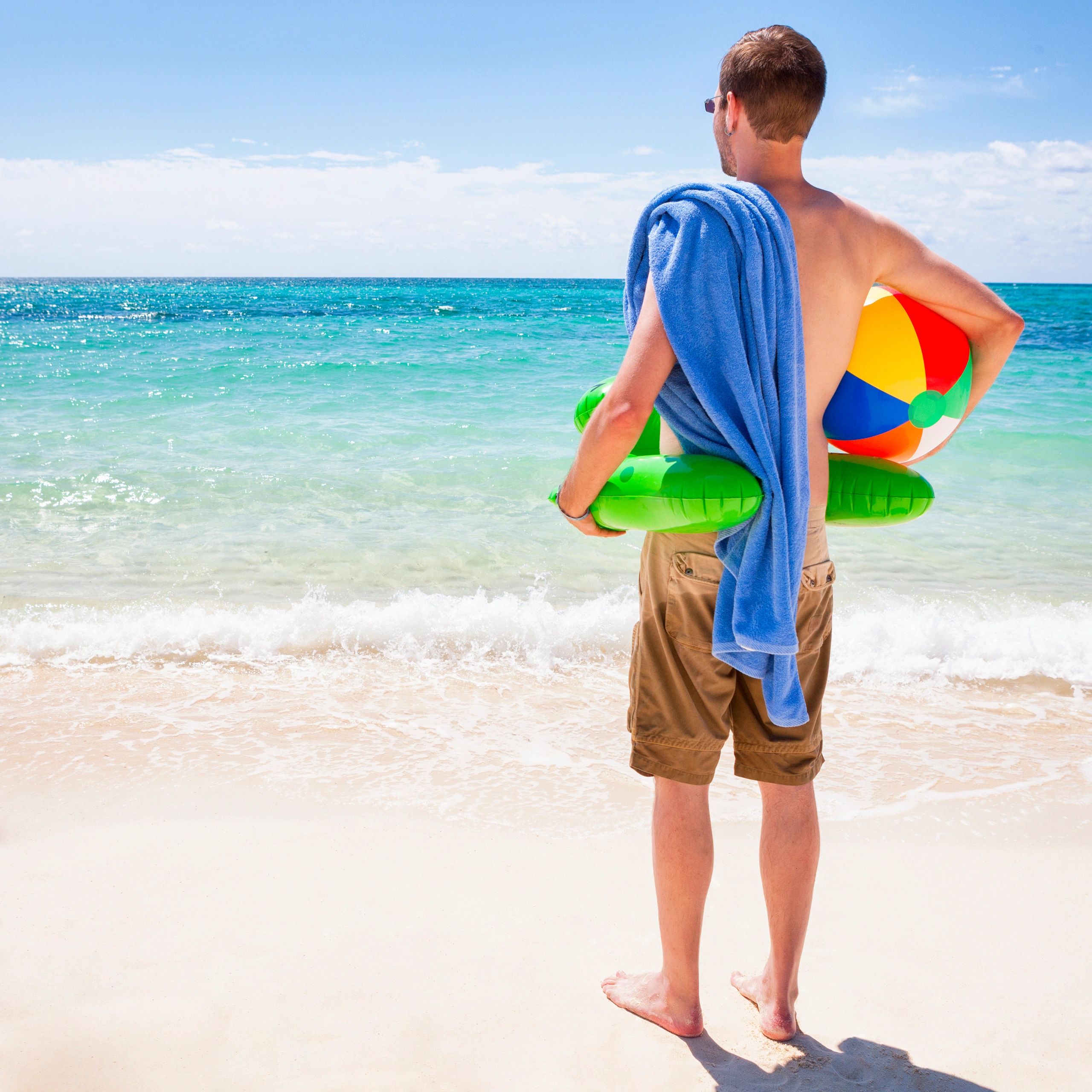 Man with floaties and towel looking at the sea on a sunny beach.