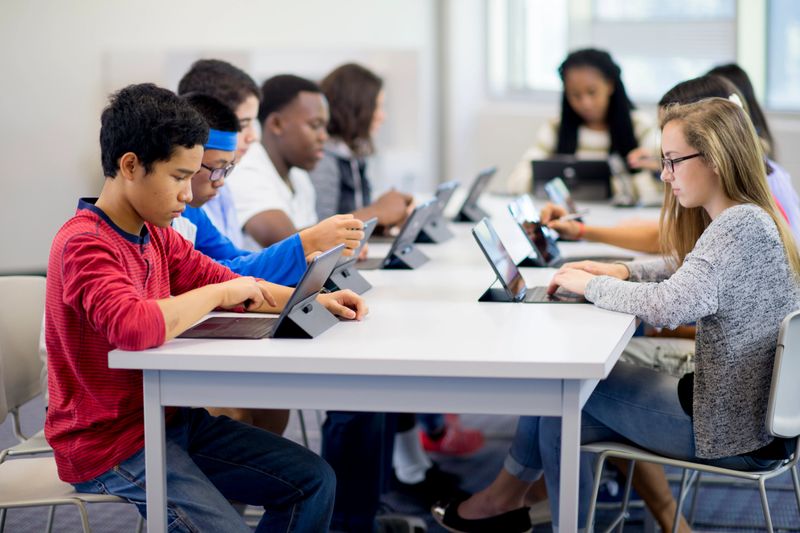 A multi-ethnic group of high school teenagers are working on digital tablets in the computer lab of the school.