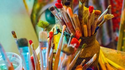 A collection of colorful paintbrushes in jars and a vase.