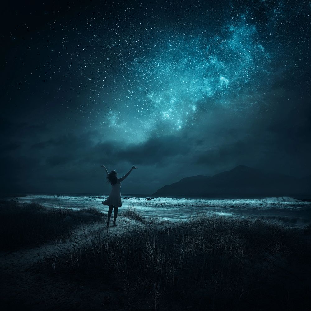 A woman in a white dress stands on a beach under a star-filled night sky.