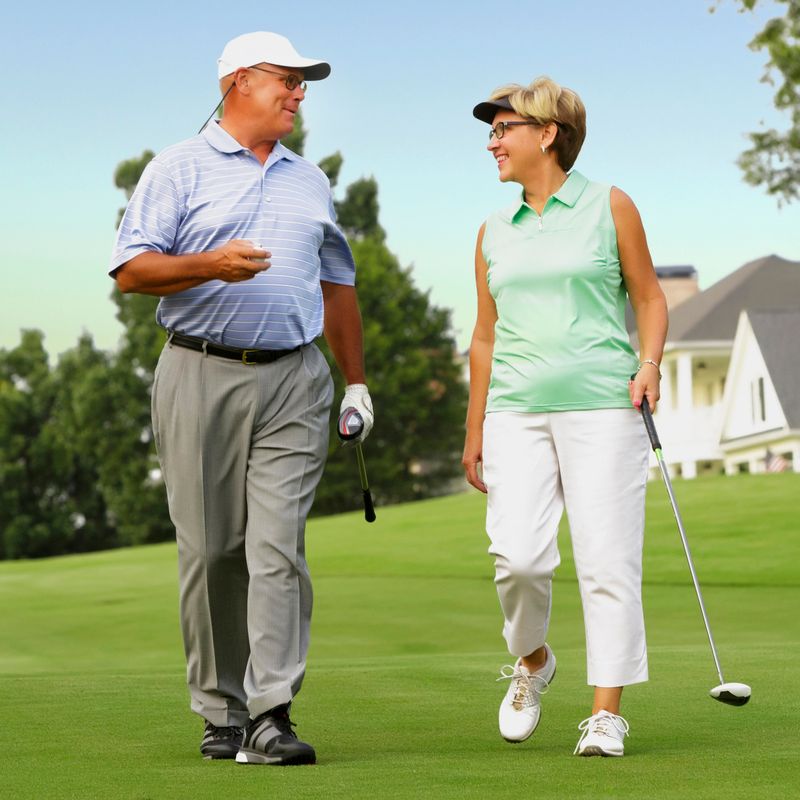 Mature couple walking a golf course carrying golf bag and golf club.