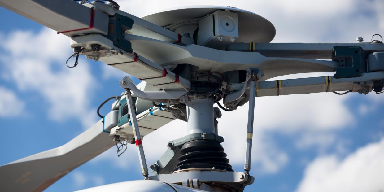 Close-up of a helicopter rotor hub and blades against a blue sky.