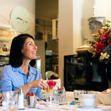 Woman smiling and pouring tea at a table.
