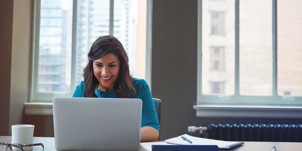 Woman happily working on a laptop in a bright office.