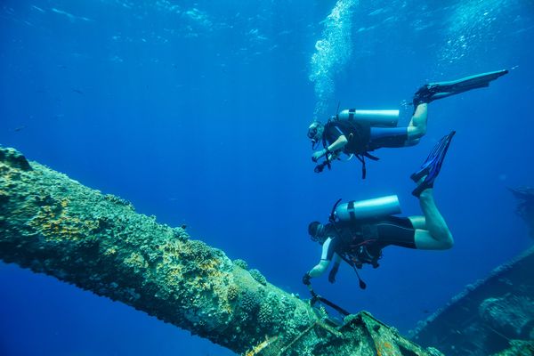 Two scuba divers exploring a coral-covered underwater shipwreck.