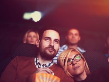 Couple enjoying a movie in a theater, sharing popcorn.
