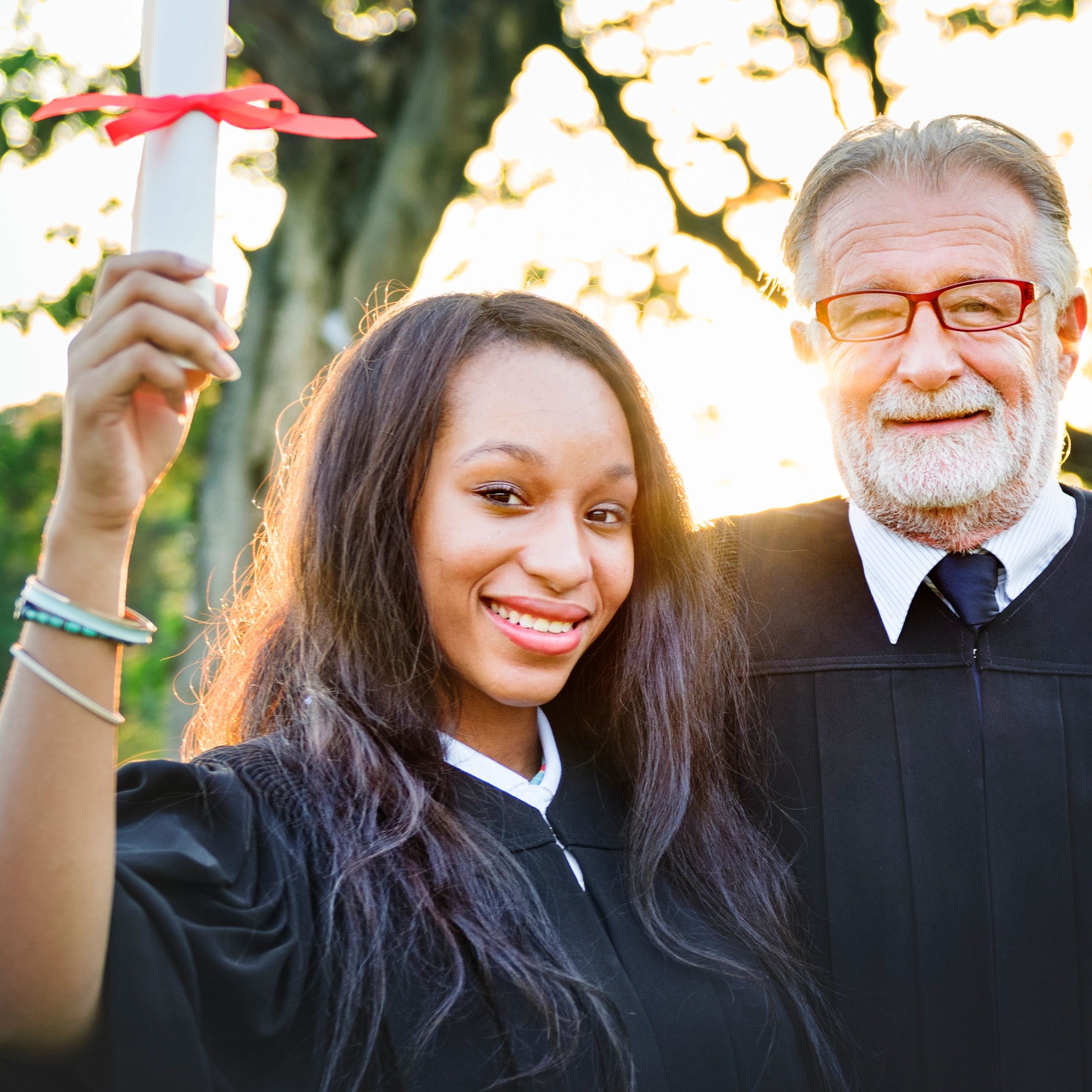 Smiling graduate holding diploma with a man beside her.