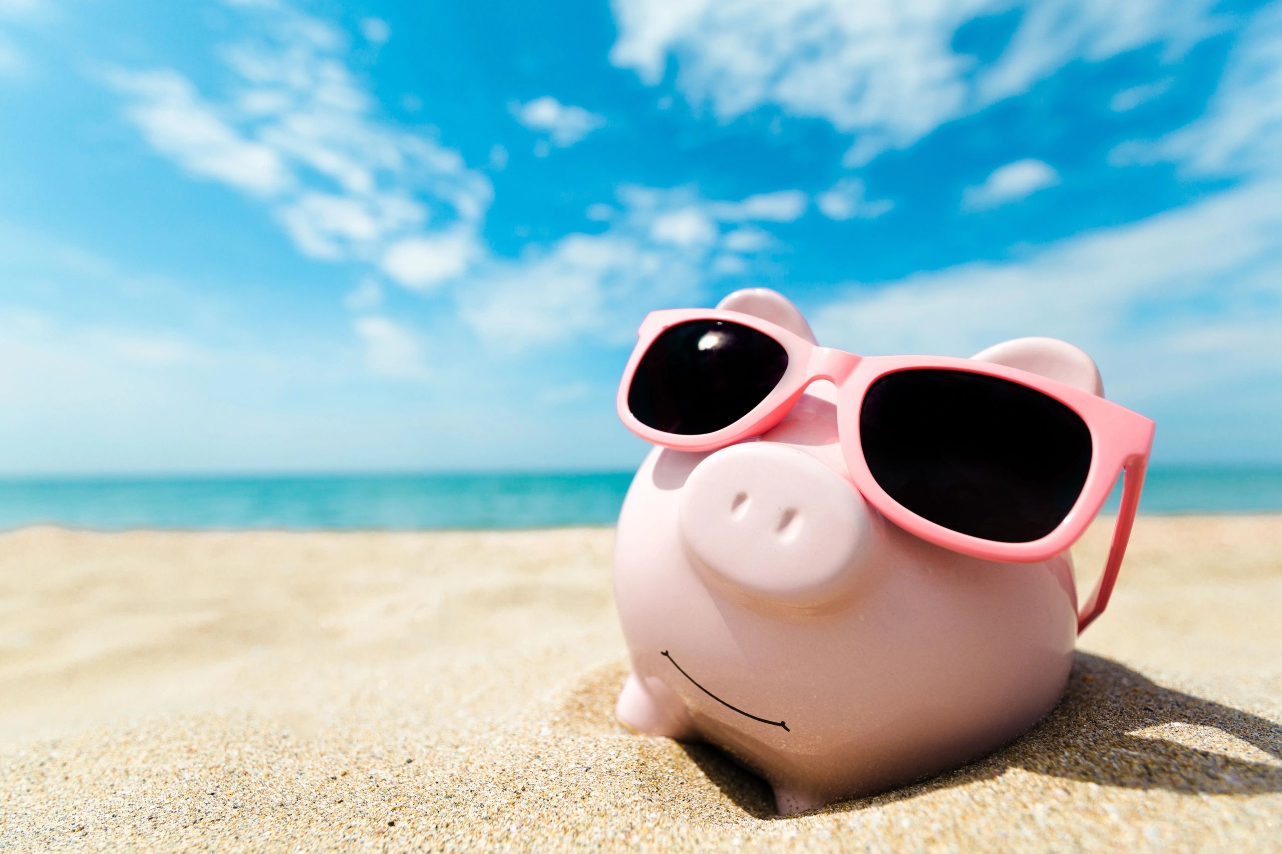 Piggy bank with sunglasses on a sunny beach.