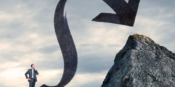 Businessman contemplating a twisting arrow pointing to a mountain peak.