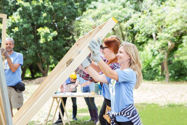 Women working together lifting wooden boards outdoors.