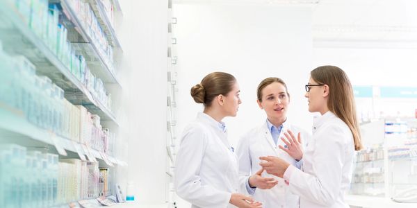 Three pharmacists discussing in a pharmacy aisle.