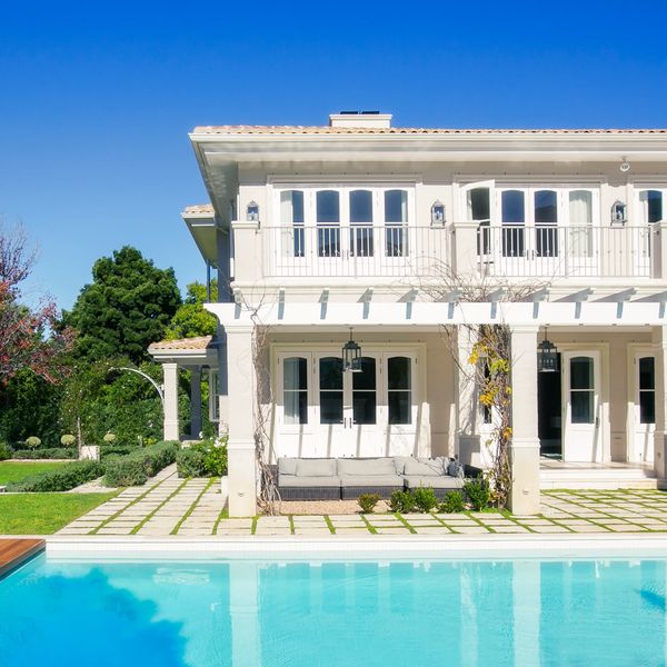 Luxurious two-story house with a pool and spacious garden under a clear blue sky.