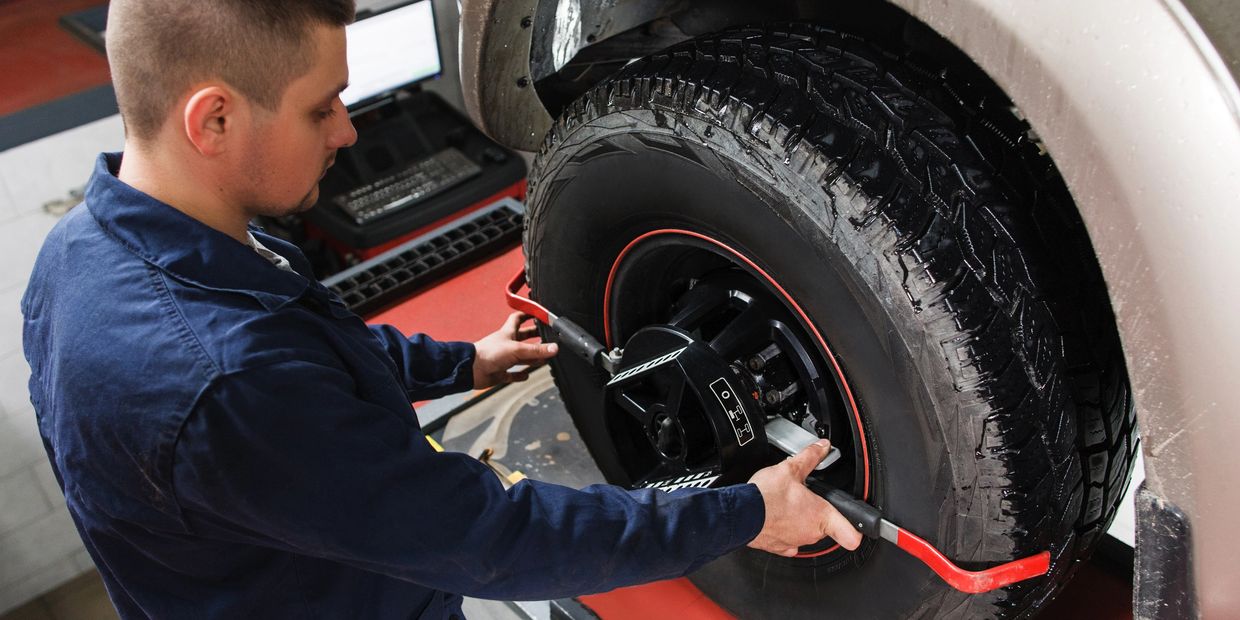 Mechanic calibrating wheel alignment on a vehicle in a workshop.