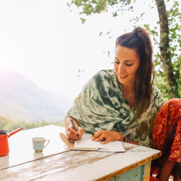 Woman writing in notebook outdoors with mountains in background.