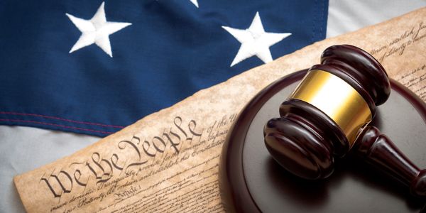 A gavel on a U.S. Constitution with the American flag in the background.