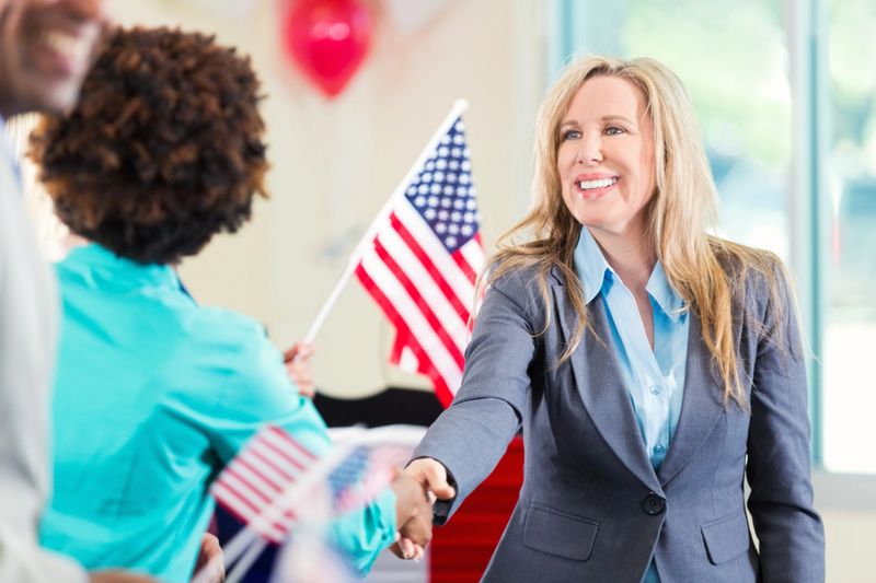 Beautiful blond politician shaking hands with an African American woman in teal.