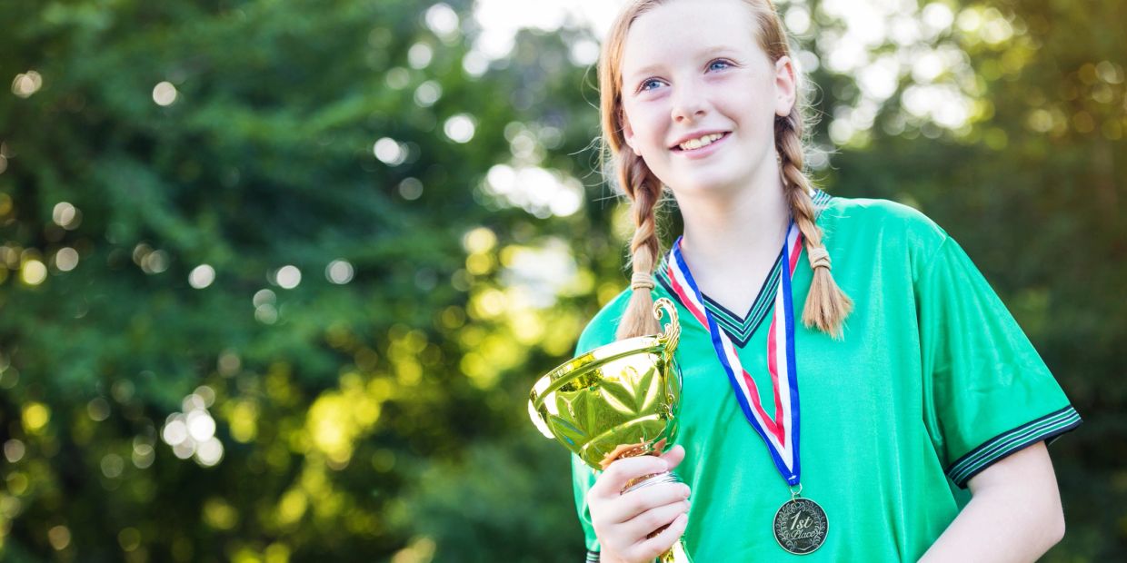Smiling girl holding a trophy and wearing a medal.