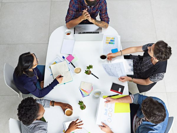 Four people collaborating around a white table with documents and coffee.