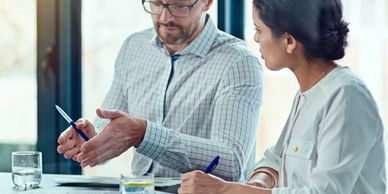 Two colleagues discussing work with pens and papers at a table.