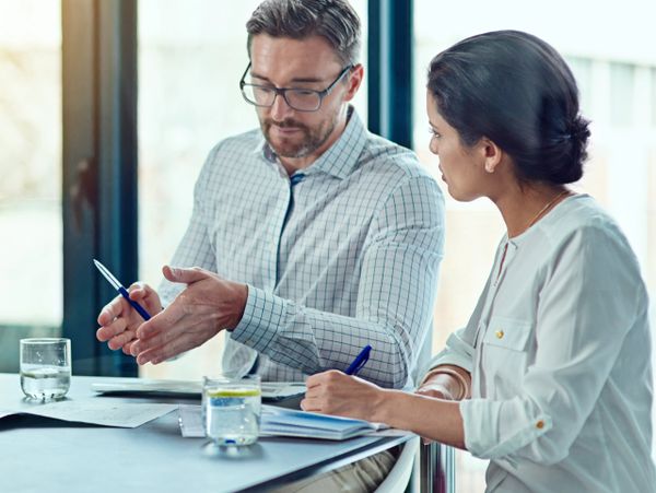 Two professionals discussing work at a table with documents and water glasses.