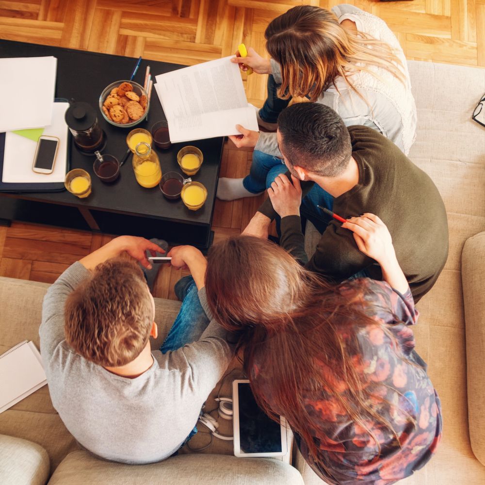 Four people studying together with drinks and snacks on the table.