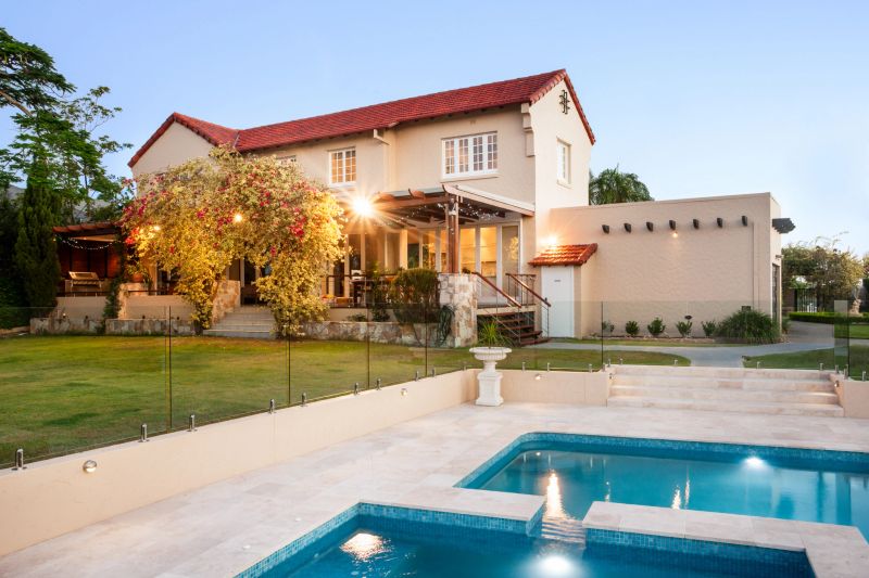 Modern mansion decorated with natural items like yellow trees and vines beside green grass lawn, garden and pool from the front