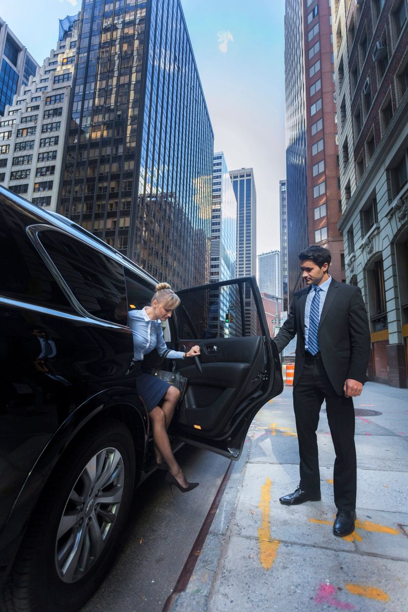 Young business woman getting out of a luxury car while a man is holding the door open for her in downtown New York City