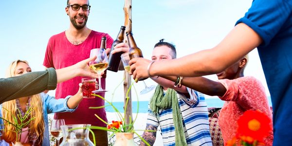 Friends clinking glasses outdoors, enjoying a sunny meal together.