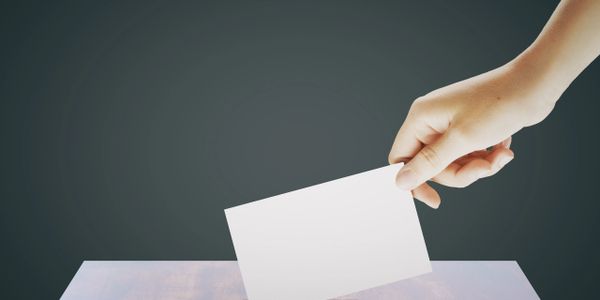 Hand placing a blank white card into a ballot box.