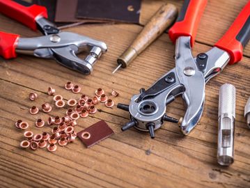 Leather crafting tools and copper rivets on a wooden surface.