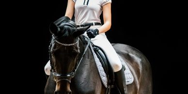A rider in white attire on a black horse against a black background.