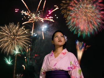 Woman in traditional attire watches vibrant fireworks at night.