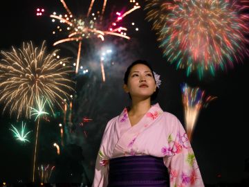 Woman in traditional attire watches vibrant fireworks at night.