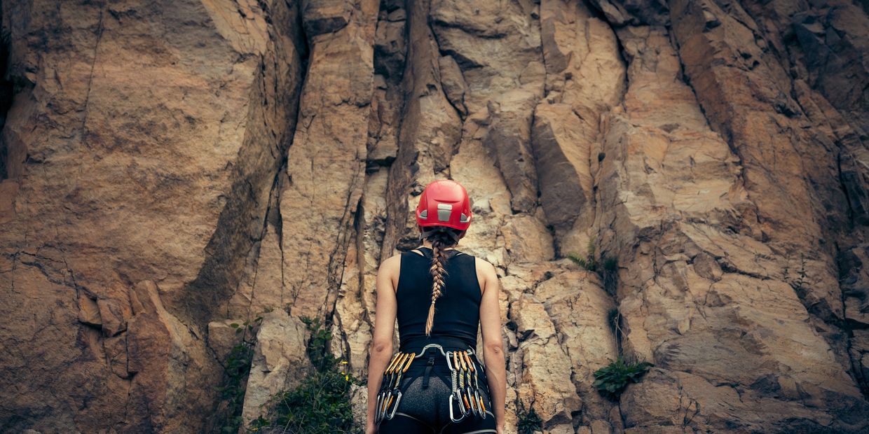 Female rock climber in climbing gear looking up at a rock wall.