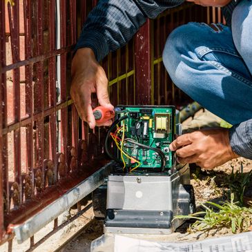 Technician repairing an automated gate motor outdoors with tools.